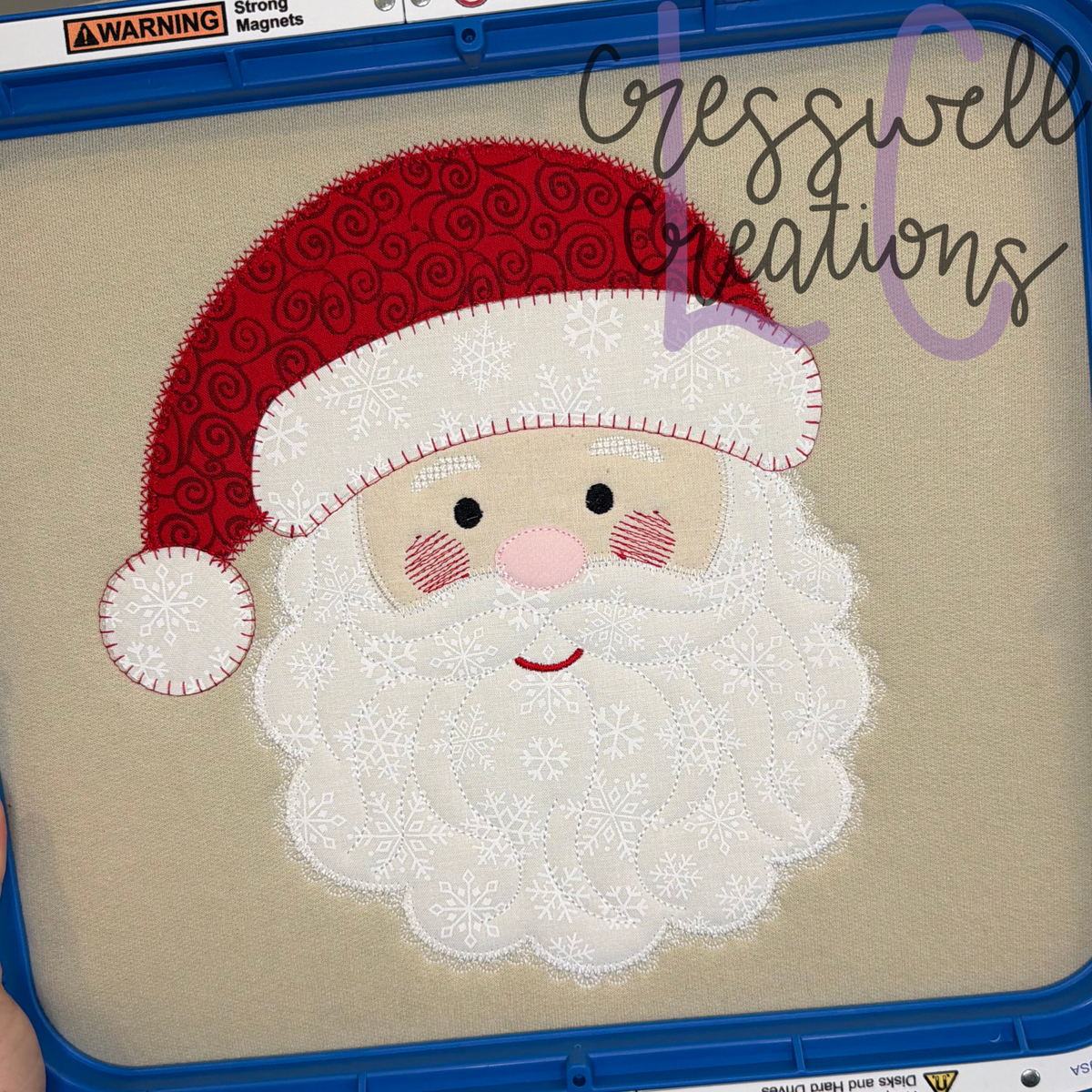 Santa face applique with a red sequin hat and white fluffy beard, stitched in an embroidery hoop